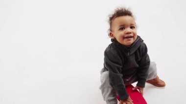 Kıvırcık saçlı küçük Afro-Amerikalı çocuk kaykayla oynuyor. Tam çekim stüdyosu var. Arka planda gri fotokopi alanı var. 