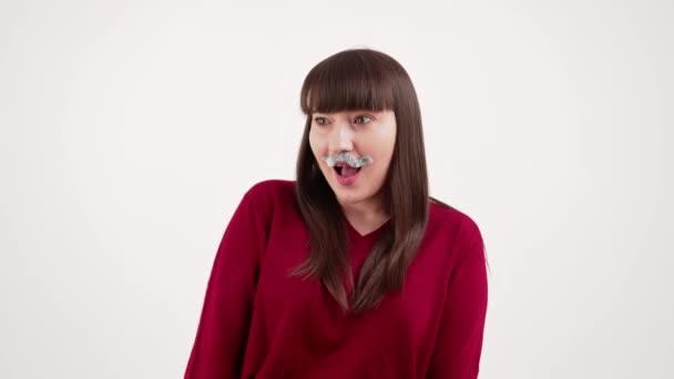 Rolig kaukasisk kvinna med rakt brunt hår och lugg bär falska grå mustasch och gör roliga ansikten till kameran. Isolerad studio skott med vit bakgrund. — Stockvideo