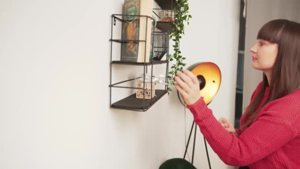 Millennial Kaukasische vrouwelijke interieur ontwerper versieren witte muur met kleine objecten. Binnenhuisconcept. — Stockvideo