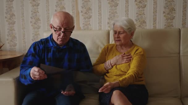 Ustaraný důchodce pár sedí na pohovce a dívá se na rentgen výsledky střední plné záběr vnitřní nemoc koncept — Stock video