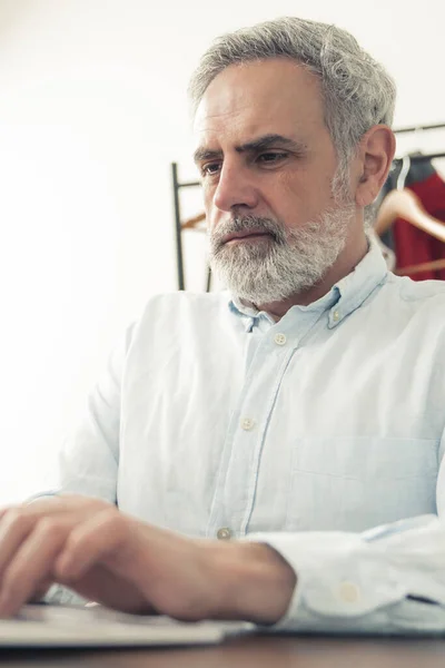Verticale indoor shot van een gefocuste oudere man met grijs haar, met een baby blauw shirt en toetsenbord. Werkconcept. — Stockfoto