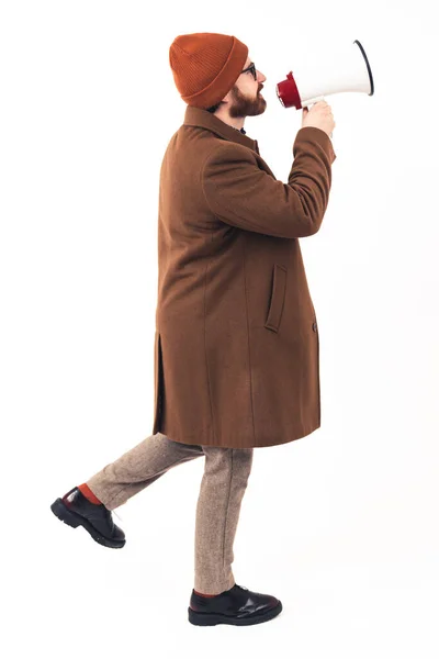 Vertical full body studio shot de un hombre caucásico barbudo con un abrigo marrón y un gorro sosteniendo el altavoz y anunciando las próximas ventas. —  Fotos de Stock