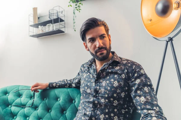 Wealthy sexy businessman sitting on the green quilted sofa with stylish lamp in the background — Stock Photo, Image