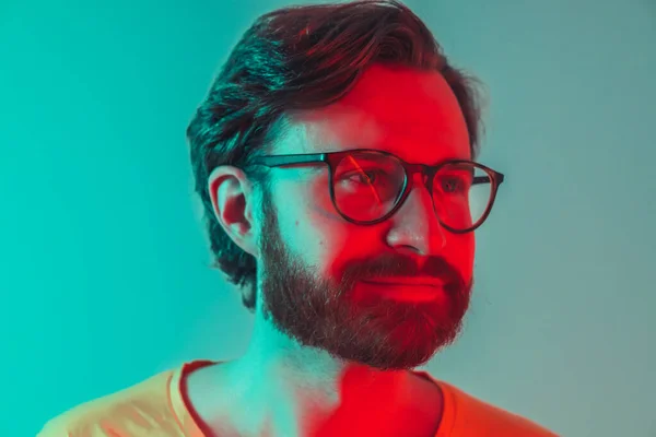 Портрет задумчивого молодого европейского бородатого человека в новых очках с красным неоновым светом на лице. Реклама очков. — стоковое фото