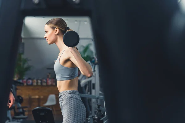 Menina bonita em sportswear cinza fazendo agachamentos com halteres no ginásio — Fotografia de Stock