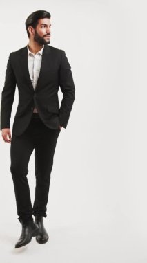 Dikey stüdyo, beyaz arka planda smokin giyen ve elini bir yöne doğru kaldırıp işaret eden Latin, baştan çıkarıcı, neşeli bir adamın çekimini yapıyor. Uzayı kopyala Yüksek kalite 4k görüntü