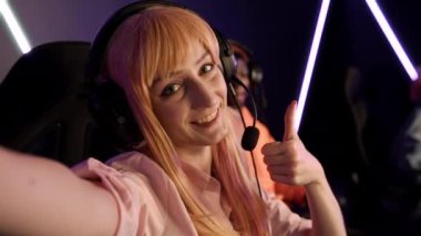 Online bir oyun etkinliği sırasında kafasında büyük kulaklıklarla oyun sandalyesinde oturan neşeli, beyaz bir kadın. Yüksek kalite 4k görüntü