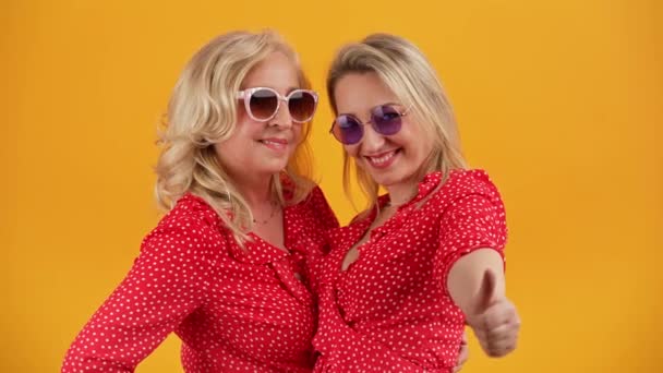 演播室中拍摄了两个40多岁的白人妇女的橙色背景 她们穿着同样的衣服 戴着同样的太阳镜 互相笑着拥抱 高质量的4K镜头 — 图库视频影像