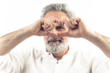 60 'lı yaşlarda Avrupalı çekici bir adamın beyaz arka planda çekimleri, parmakları yüzünde kalp işareti yapıyor. Ön plana odaklan. Yüksek kalite fotoğraf