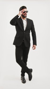 Güneş gözlüklü, kolları ve bacakları çapraz duran zarif, seksi Latin bir genç. Stüdyo fotoğrafı, beyaz arka plan. Yüksek kalite 4k görüntü