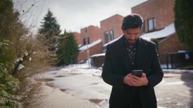 Yatay açık hava çekimi. 20 'li yaşlarda Latin seksi, iyi giyimli bir adam bir caddenin yanında duruyor, akıllı telefonuyla mesajlaşıyor. Yüksek kalite 4k görüntü
