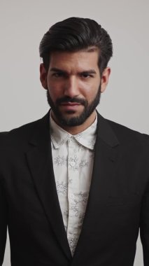 Smokin giymiş, kollarını göğsüne bağlayan, ciddi anlamda öfkeli, Latin bir iş adamı. Beyaz arka planda dikey orta stüdyo çekimi. Yüksek kalite 4k görüntü