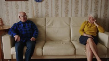 Kıdemli ilişki sorunları konsepti. İki yaşlı Avrupalı emekli çift, eski usul rahat bir dairede deri bej bir koltukta oturuyor. Yüksek kalite 4k görüntü