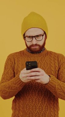 Bere takmış, akıllı telefonuyla kazak ören Avrupalı bir gencin dikey çekimleri. İnternetten alışveriş konsepti. Yüksek kalite 4k görüntü