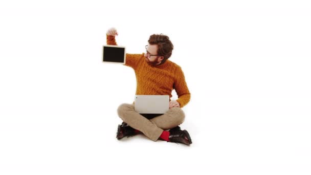 ひげを生やした白人青年は 膝の上にモックアップの黒板とノートパソコンを持っていた 白い背景スタジオのショットコピースペース 高品質4K映像 — ストック動画