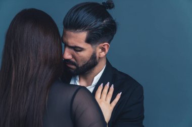 Siyah saçlı, takım elbiseli yakışıklı bir adam uzun tırnaklı uzun saçlı bir kadına yaklaşıyor. Karanlık arka planda stüdyo portresi. Sınır kavramı. Yüksek kalite fotoğraf