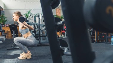 Esmer, zayıf, yirmili yaşlarda, sürekli neşeli, gri spor giyimli, modern bir spor salonunda hafif bir halter kaldıran bir kadın. - Evet. Yüksek kalite fotoğraf