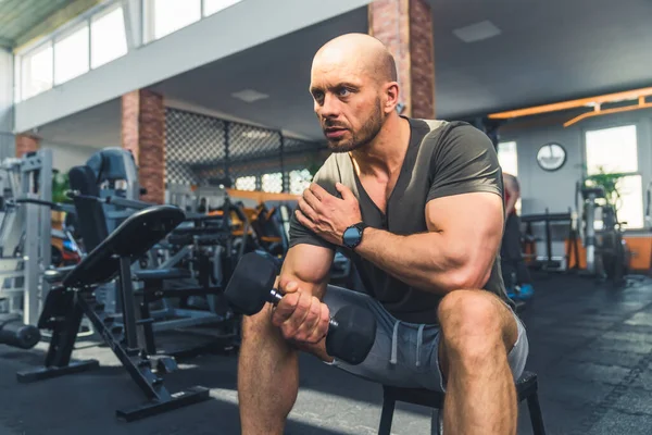 Muscular caucasian middle-aged bald man in sports clothes lifting the dumbbell at gym. Wellness and physical strength concept. High quality photo