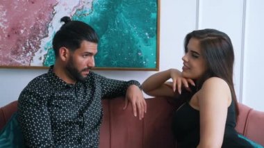 Uzun saçlı, siyah kolsuz tişörtlü güzel beyaz kadın oturma odasında kanepede dinlenirken sakallı, yakışıklı kocasına baştan çıkarıcı bir şekilde bakıyor. Yüksek kalite 4k görüntü