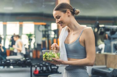 Spor kıyafetli genç bir kadın ve omuzunda bir havlu spor salonunda dengeli bir salata yiyor. Yüksek kalite fotoğraf