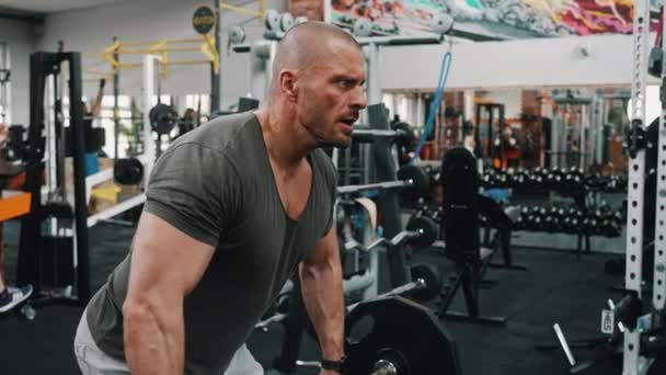 集中的千年秃头肌肉男举起一个沉重的杠铃用他的三头肌 室内射击在一个健身房 高质量的4K镜头 — 图库视频影像