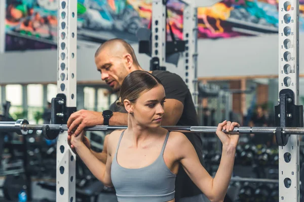 Young professional trainer man helping out a beautiful caucasian woman with weightlifting. Gym concept. High quality photo