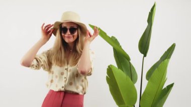 Yaz zamanı. Beyaz tenli, uzun saçlı, noktalı tişörtlü bir kadın, bir adam ve güneş gözlüğü büyük bitkinin yanında duruyor ve poz veriyor. Yüksek kalite 4k görüntü