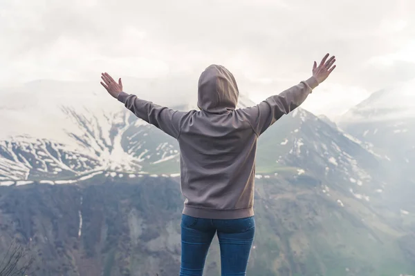 Freedom concept. Young unrecognizable person in a gray hoodie spreading their arms while standing in front of a beautiful heavenly Mountain View. High quality photo