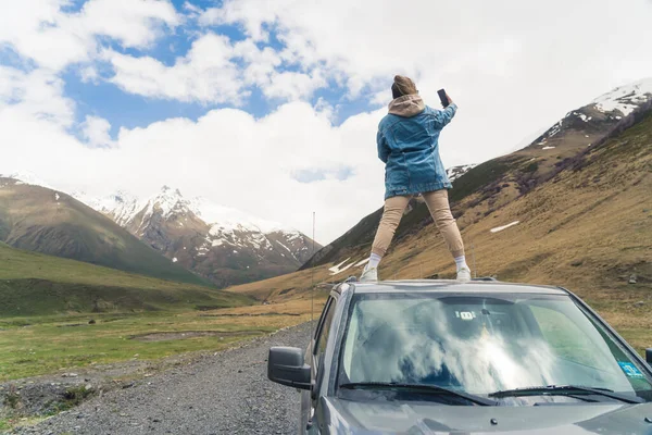 Its time for adventure. Unrecognizable person in casual clothing standing on the rooftop of a car in order to take selfies with a beautiful view. High quality photo