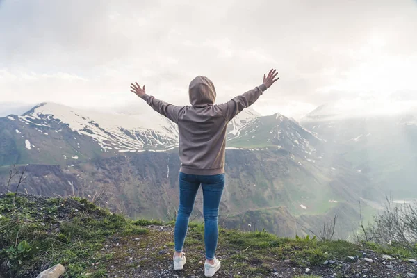 Unrecognizable person in a gray hoodie and blue jeans spreading their arms while standing up in the mountain. Beautiful mountain view. High quality photo