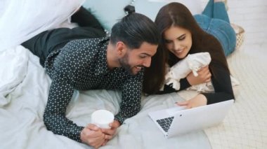 Aşk ve ilişkiler kavramı. Uzun saçlı, sıradan kıyafetler giyen çekici genç kız internette seksi sakallı erkek arkadaşına bir şeyler gösteriyor. Yüksek kalite 4k görüntü