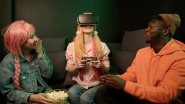 Bir internet kafedeki kanepede oturan üç arkadaş grubu. Bir tanesi profesyonel VR gözlükleri ve bilgisayar oyunları denetleyicisi kullanıyor. Bağ kurma, arkadaşlık kurma. Yüksek kalite 4k görüntü
