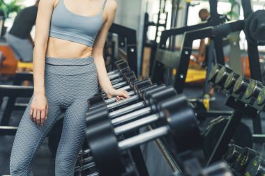 Spor sutyen ve desenli tayt giyen beyaz tenli kadın büyük bir dambıl almaya çalışıyor. Kapalı çekim. Yüksek kalite fotoğraf