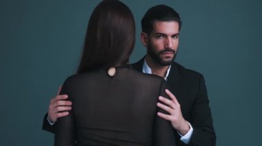 Takım elbiseli seksi, baştan çıkarıcı sakallı adam iki eliyle uzun saçlı kadınını sıkıca tutuyor. Gri arka plan stüdyo. Yüksek kalite 4k görüntü