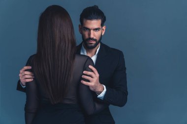 Öfkeli, baskın, yakışıklı, 30 'lu yaşlarında sakallı Kübalı adam uzun saçlı kadınını uzun kollu kollarıyla sıkıca kavrayıp kameraya bakıyor. Stüdyo çekimi. Yüksek kalite fotoğraf