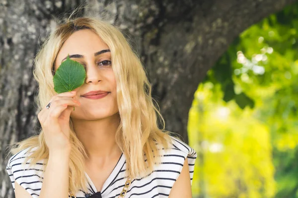 spring mood - blond Caucasian girl holding a small green leaf close to the eye. medium closeup outdoor. High quality photo