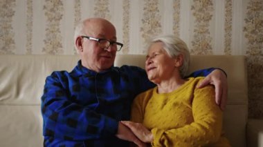 Yaşlı beyaz çift kanepede oturuyor ve geçmişten bahsediyorlar. Mutlu bir şekilde yakın plan ev içi yaşlılar destek kavramı. Yüksek kalite 4k görüntü