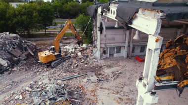 Sarı, uzun boylu bir kazıcı, büyük, eski, beyaz bir binayı yıkıp, etrafa bir sürü enkaz bırakıyor. Yüksek kalite fotoğraf