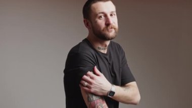 30 'lu yaşlardaki beyaz adam kollarını kaldırıyor ve kollarındaki gri arka plandaki dövmeleri gösteriyor. Yüksek kalite 4k görüntü