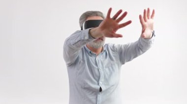 50 'li yaşlarda gri saçlı bir adam ellerini VR gözlük takarak hareket ettiriyor. Stüdyoda orta ölçekli beyaz arka plan. Yüksek kalite 4k görüntü