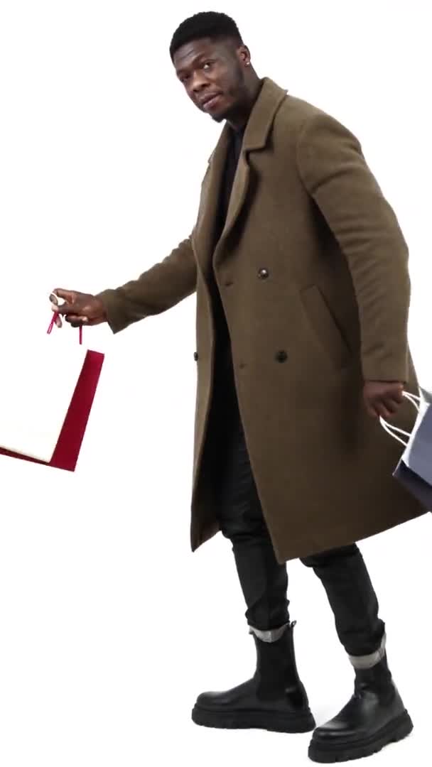 ショッピングバッグ垂直ビデオ隔離された白い背景フルショットと茶色のコートフラップの若いアフリカ系アメリカ人男性 高品質4K映像 — ストック動画