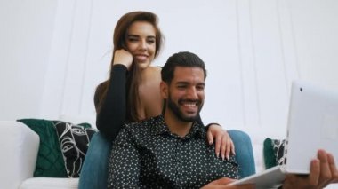 Mutlu, heteroseksüel çift, Kübalı erkek ve Kafkasyalı kadın, oturma odasında oturmuş internetten komik videolar ya da önceki yolculuklarından resimler izliyorlar. Yüksek kalite 4k görüntü