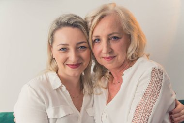 Kapalı mekanda birbirine yakın oturan, birbirine yakın oturan, kameraya bakan, şen şakrak, modaya uygun, sarı saçlı iki kadının portresi. Yüksek kalite fotoğraf