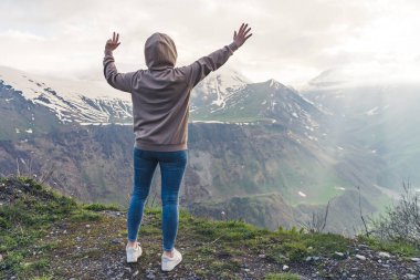 Gündelik giysiler içinde kollarını kaldırıp güzel bir dağ manzarası seyreden bir kadının arka görüntüsü. Yüksek kalite fotoğraf