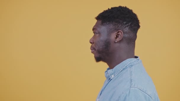 青いシャツの若いアフリカ系アメリカ人の男が離れて黄色の背景スタジオショットコピースペースを屋内で隔離見てため息をつく 高品質4K映像 — ストック動画