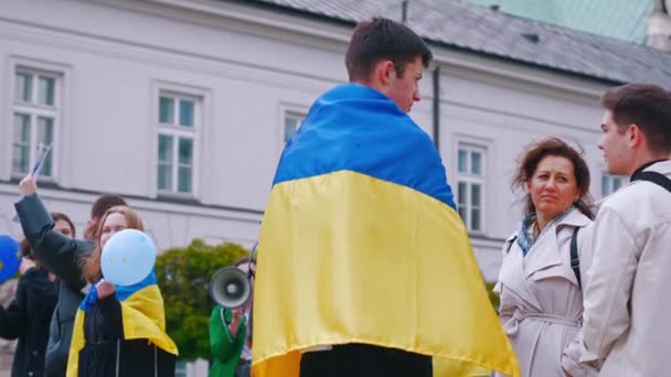 2022ポーランドのワルシャワ 親ウクライナのための平和の症状の間に白人の人々 背の高い黒髪の若い男はウクライナの青と黄色の旗で彼の背中をカバー 高品質4K映像 — ストック動画