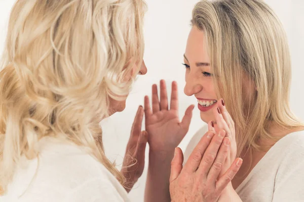 Close-up studio shot of two women with blonde hair and big smiles, standing close, touching their hands and laughing. High quality photo