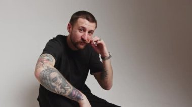 Koyu saçlı sakallı milenyum sakalı bıyığına dokunur ve yüzünü kapatır. Kollarında gri kollar olan stüdyo fotoğrafının orta boy fotokopisini çeker. Yüksek kalite 4k görüntü