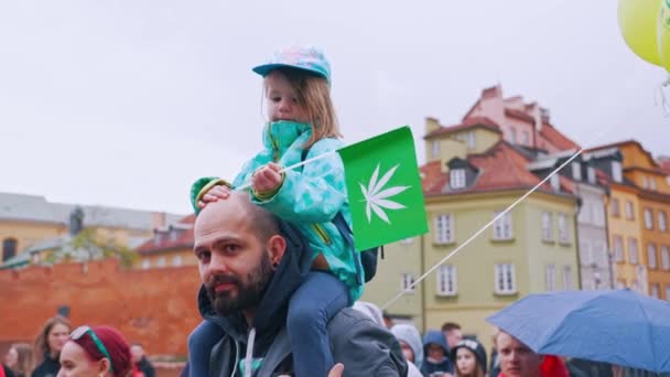 2022ポーランドのワルシャワ マリファナ合法化3月の間に父親の肩に座って雑草の葉で旗を振っている小さな女の子 そうだ 高品質4K映像 — ストック動画