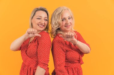 Orta yaşlı, kısa saçlı, çekici kadınlar sırt sırta durarak birbirlerine başparmaklarıyla işaret ediyorlar. Yüksek kalite fotoğraf